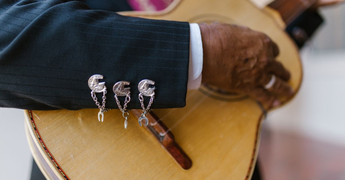 A close-up of a musician's hand strumming a traditional guitar, showcasing intricate cufflinks.